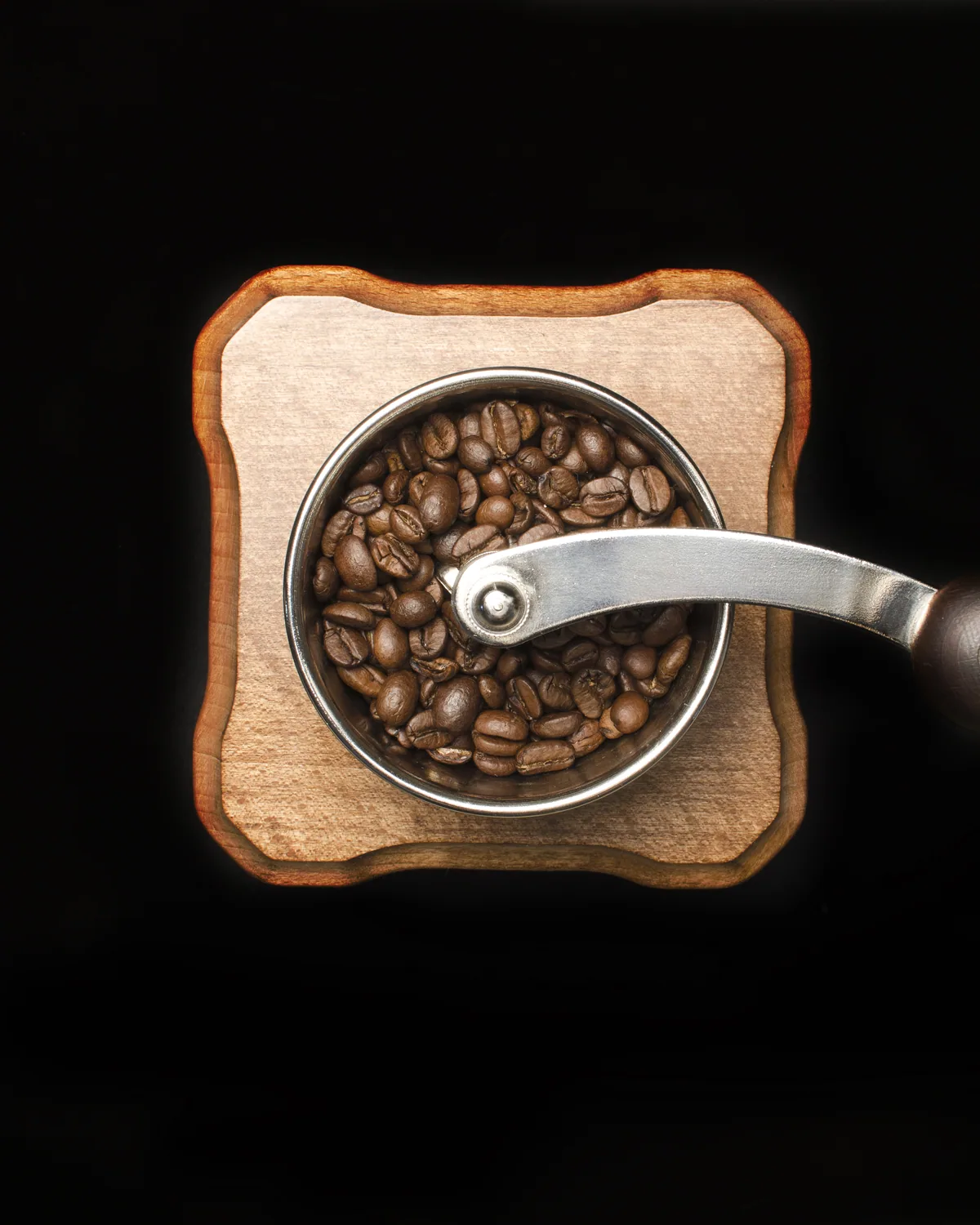 A vintage wooden box grinder with a brass hopper full of beans