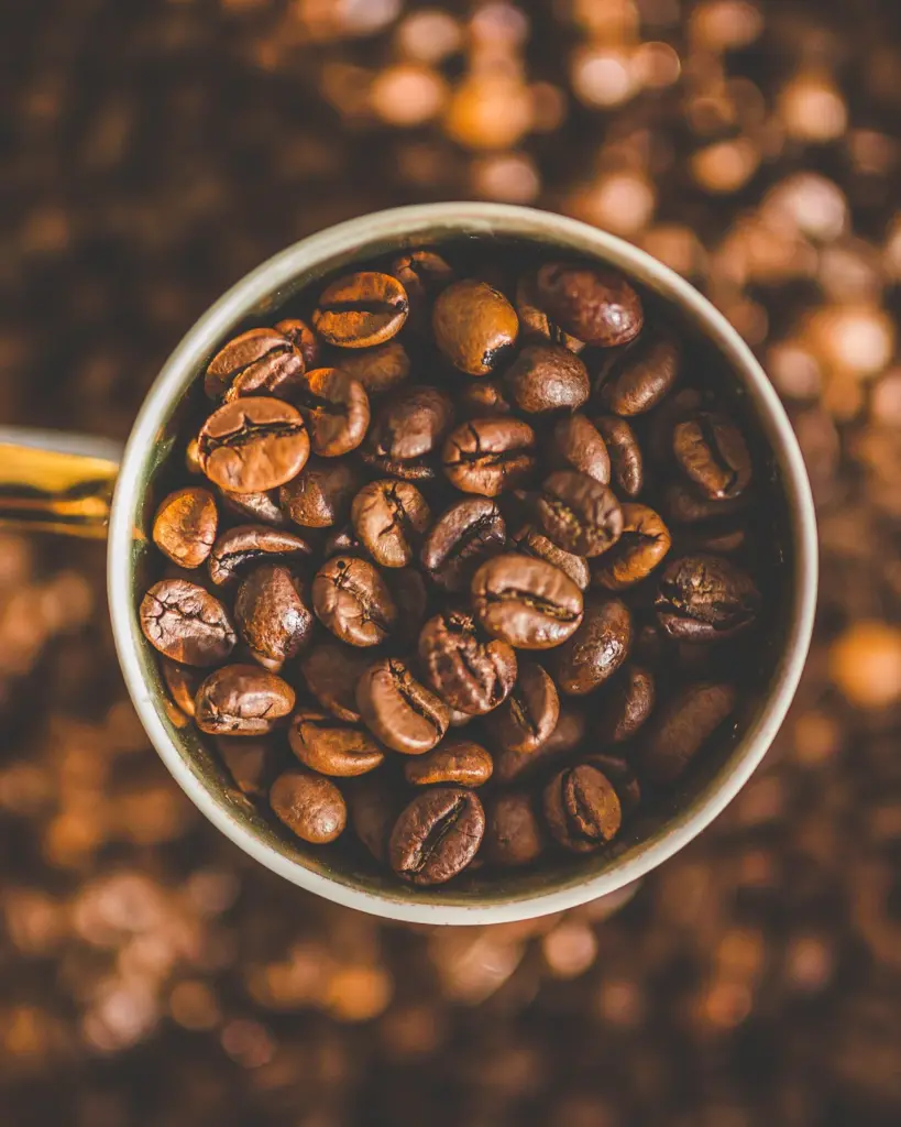A white enamel cup filled with roasted coffee beans, seen from above