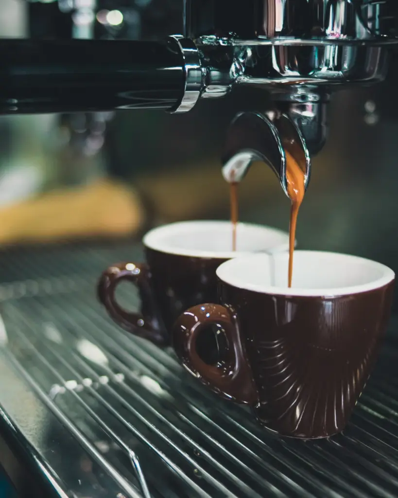 Espresso streaming from a chrome group head into two brown cups