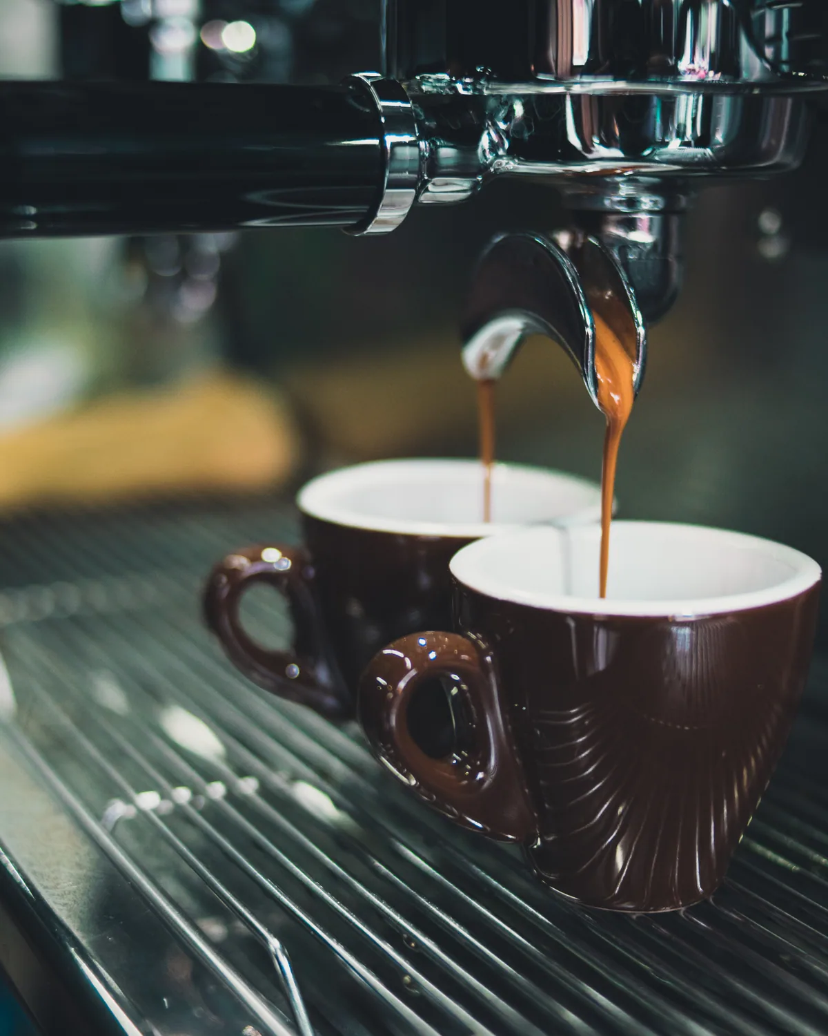 Espresso streaming from a chrome group head into two brown cups