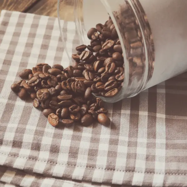 A glass jar on its side with roasted beans spilling onto checked linen