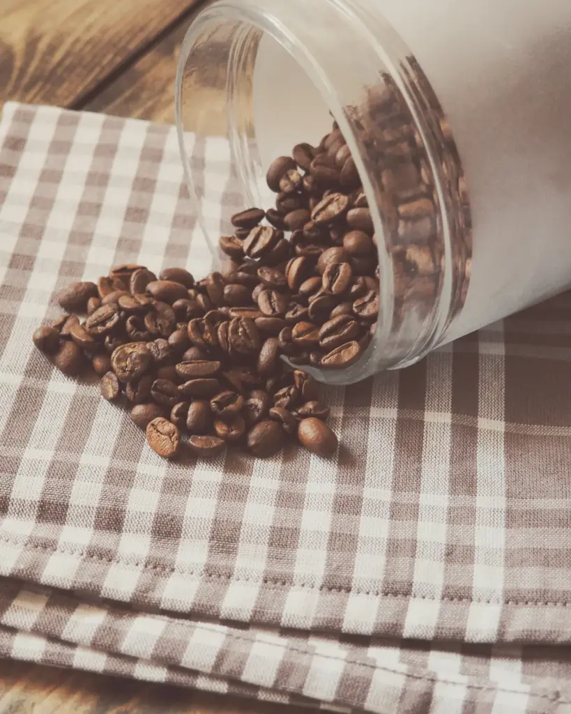 A glass jar on its side with roasted beans spilling onto checked linen