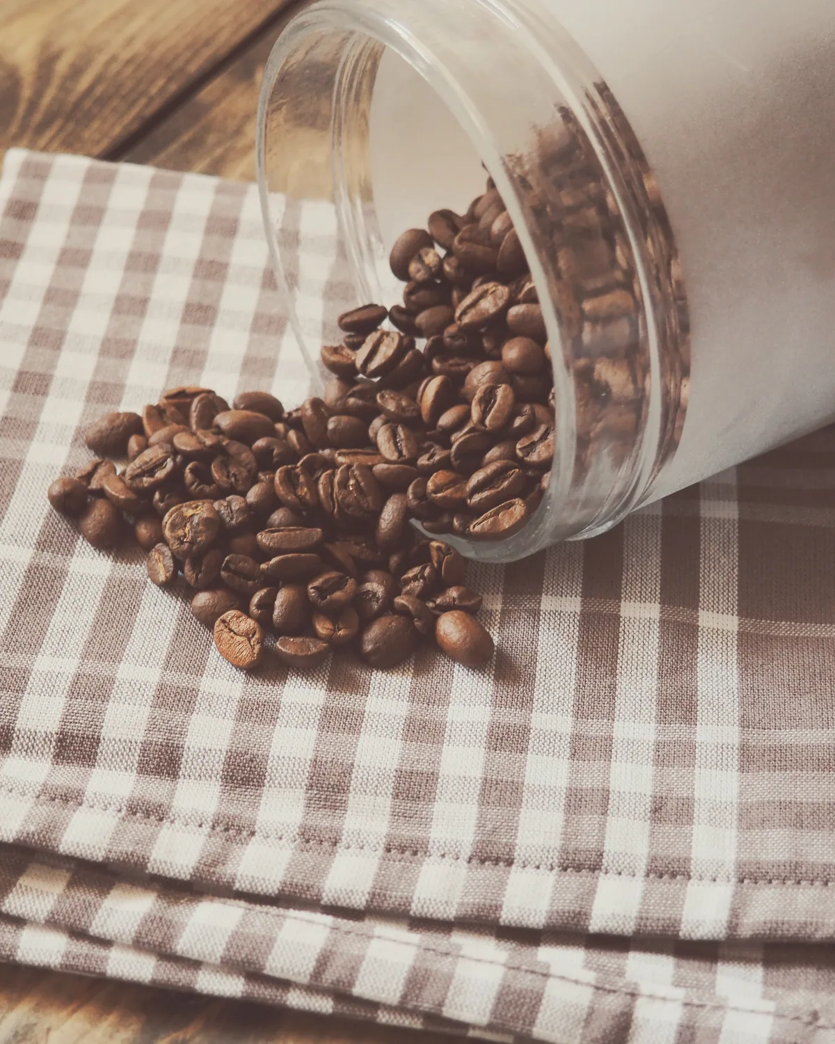 A glass jar on its side with roasted beans spilling onto checked linen