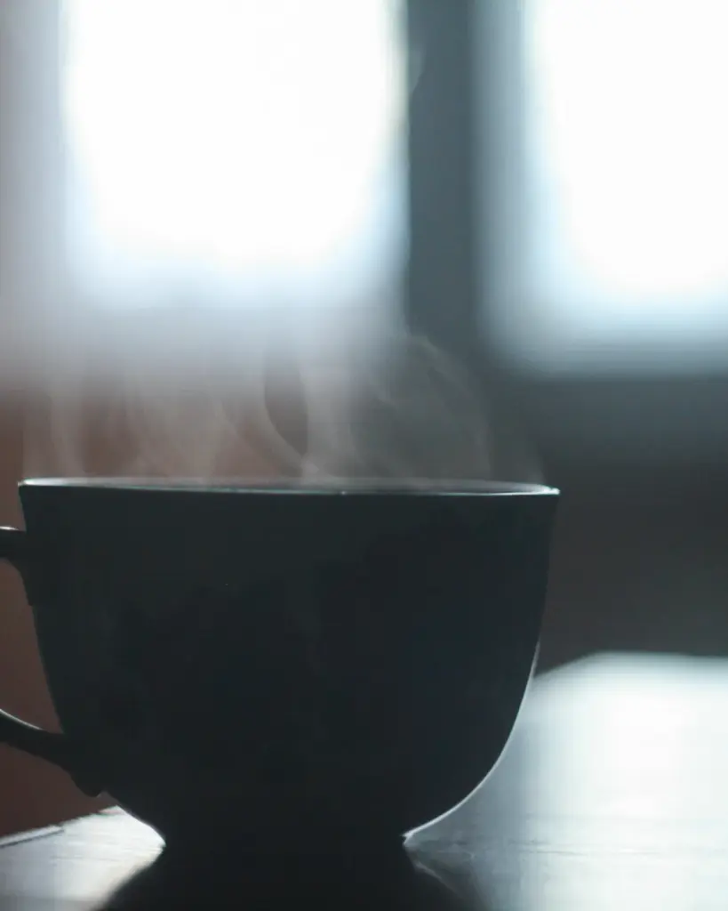 A matte black cup steaming on a dark surface against a bright window