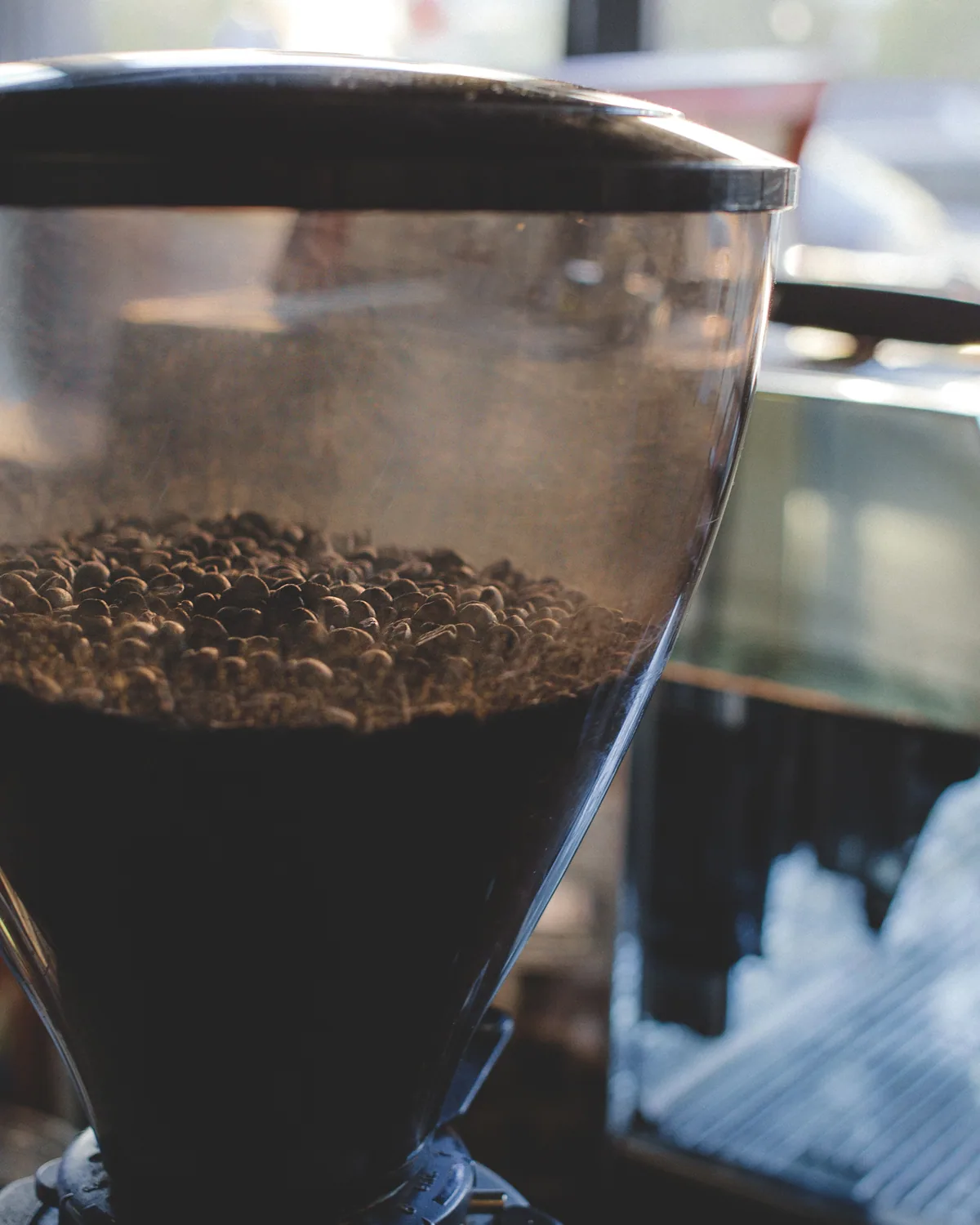 A chrome cafe grinder with a clear hopper half full of beans