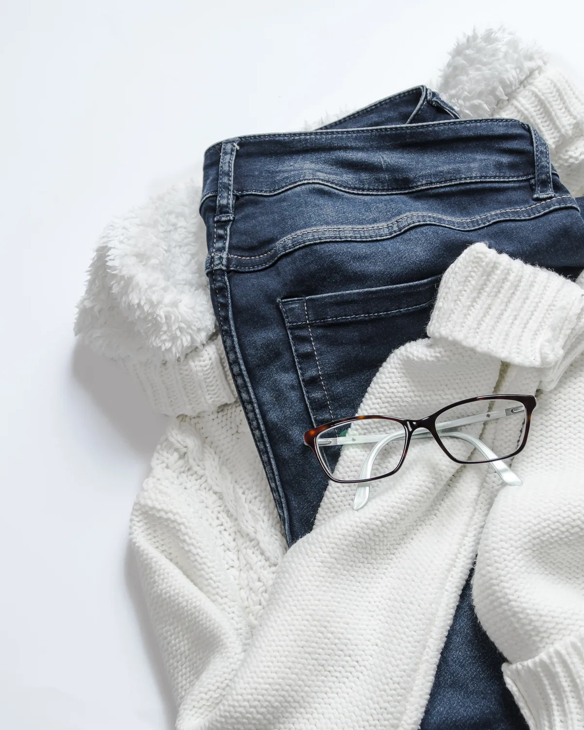 A folded cream cable-knit sweater on a white ground