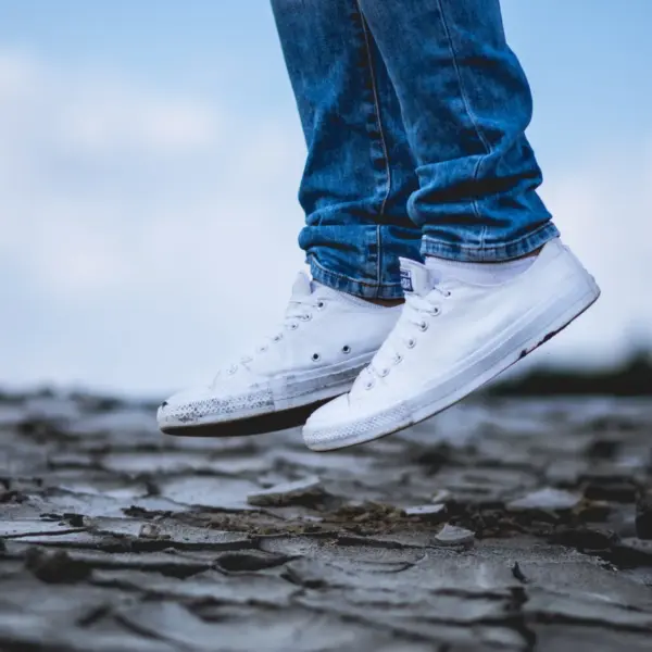 A pair of white canvas low-tops on cracked dark ground