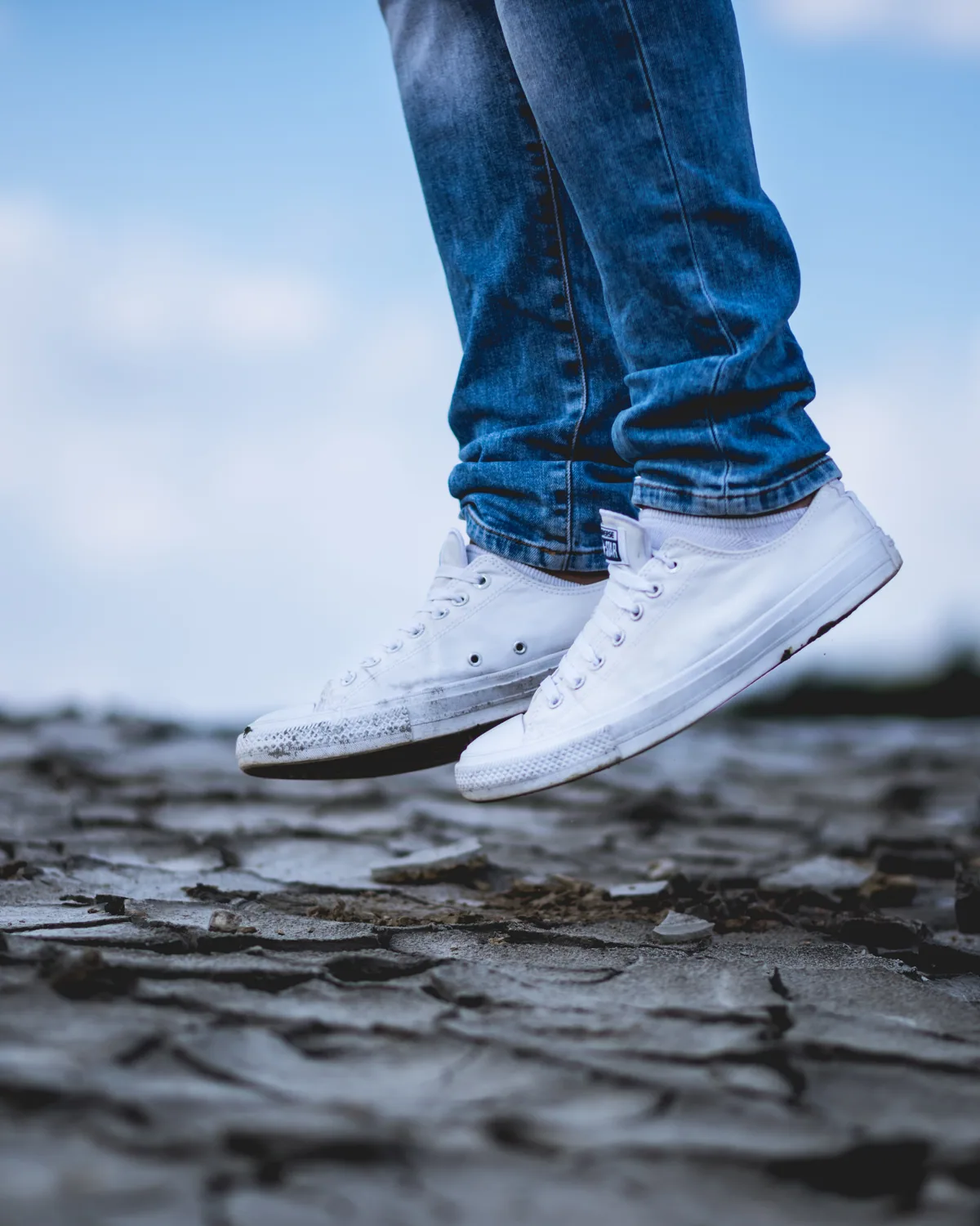 A pair of white canvas low-tops on cracked dark ground