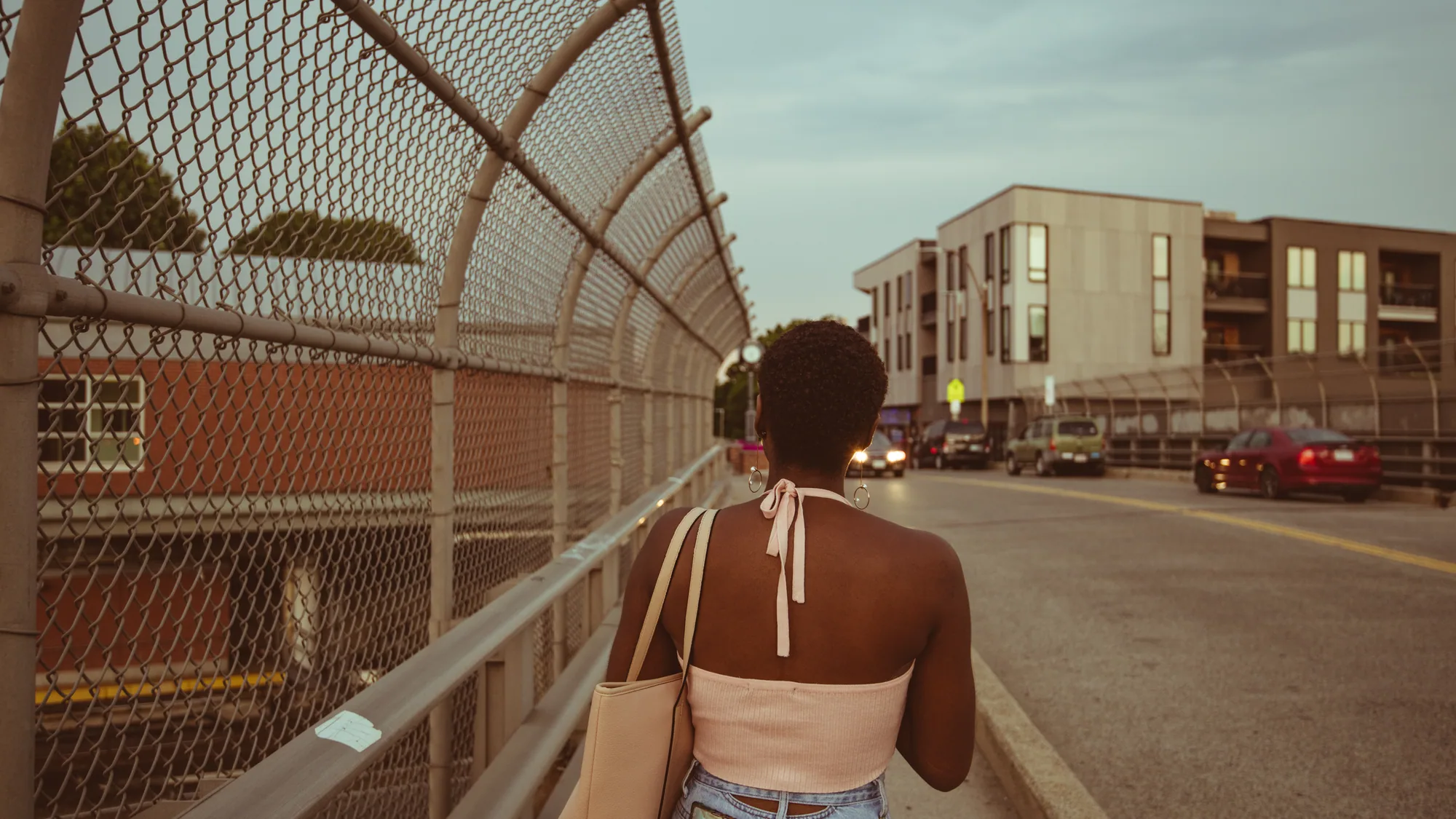 A woman walking away along a road bridge beside a tall chain-link fence