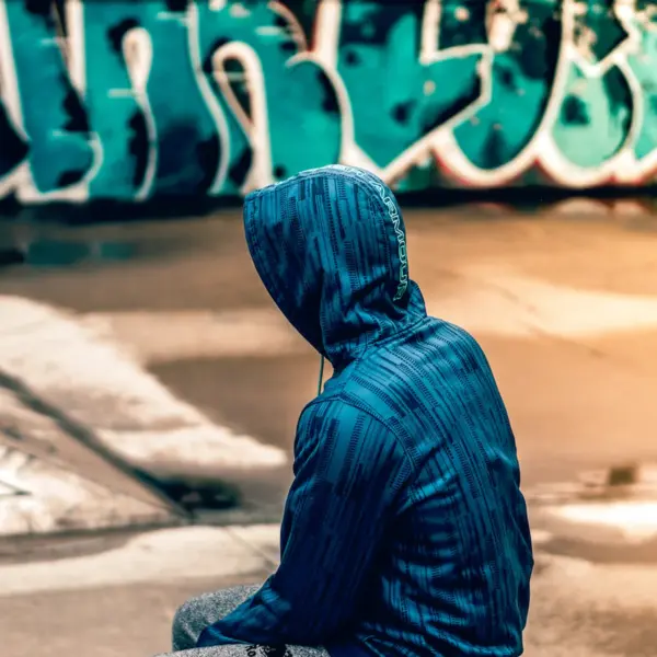 A person in a blue hooded jacket sitting on a concrete skatepark ledge