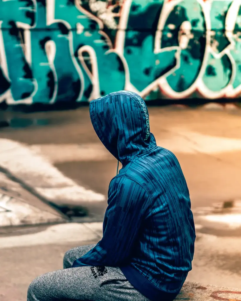 A person in a blue hooded jacket sitting on a concrete skatepark ledge