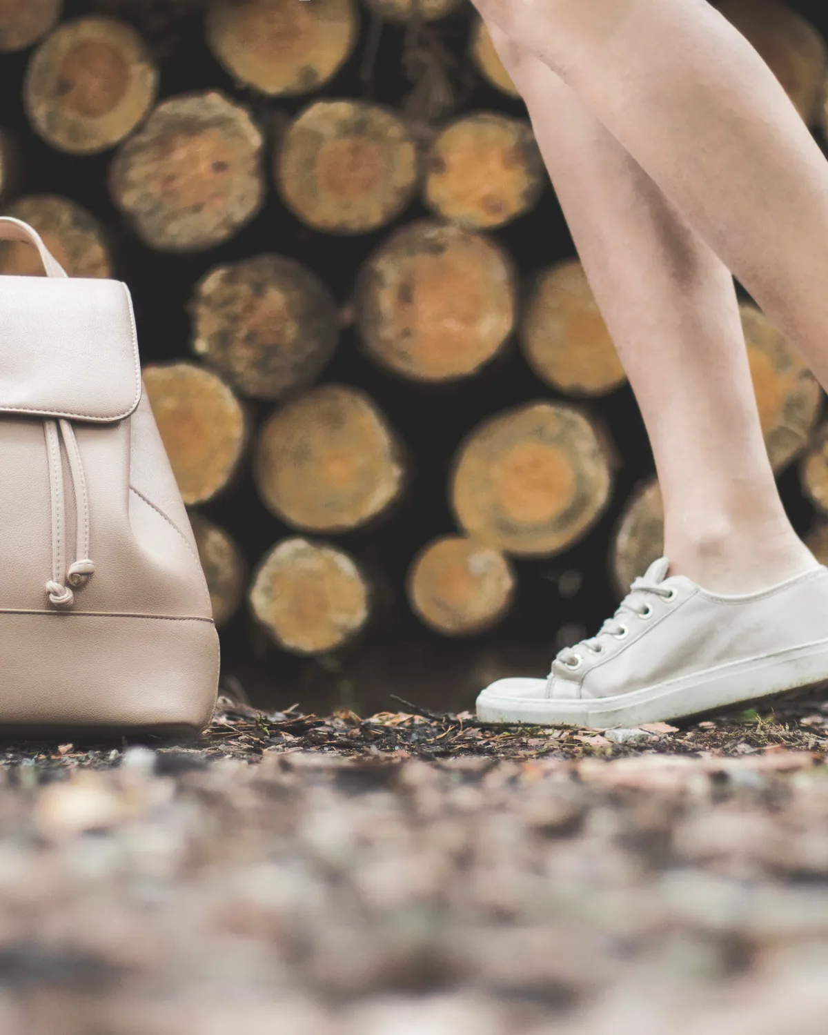 A pale grey leather backpack hanging against stacked logs