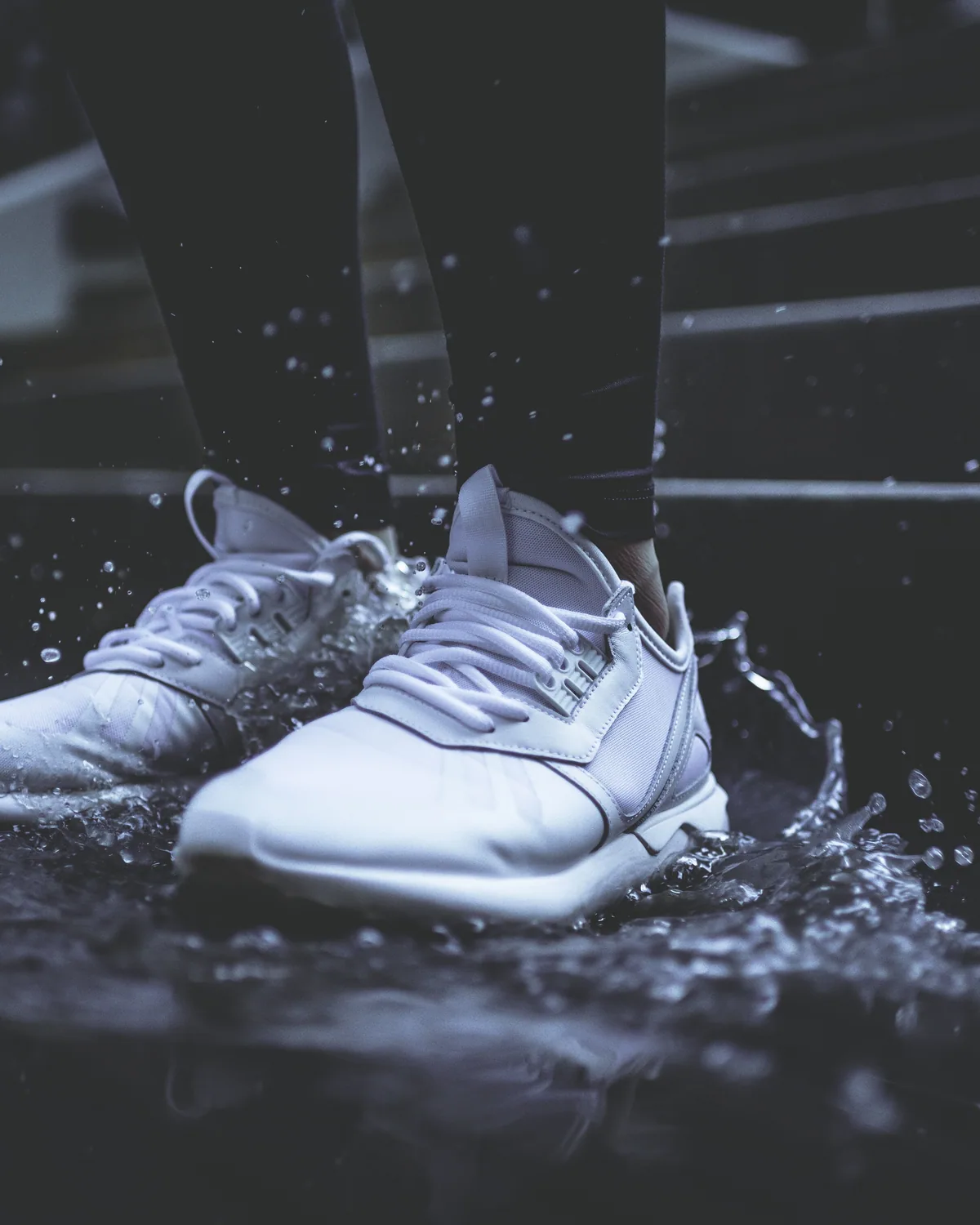 White leather sneakers landing in a puddle, water flying