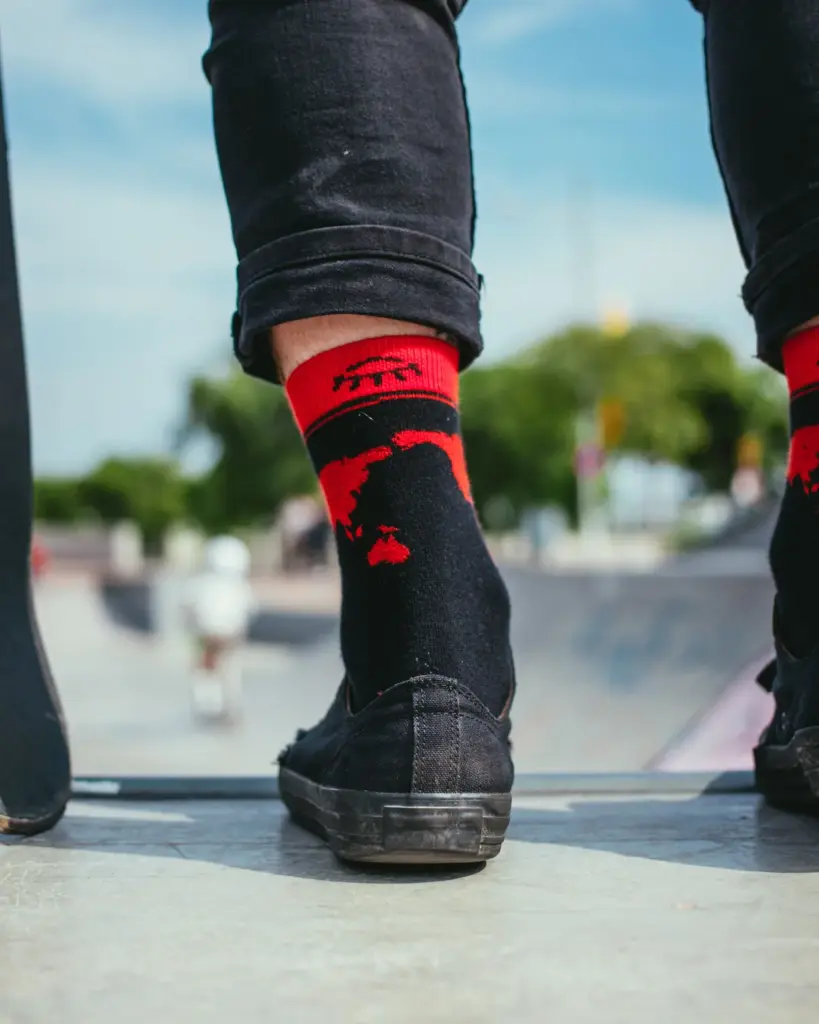 Black sneakers and red ribbed socks on a skateboard at a skatepark
