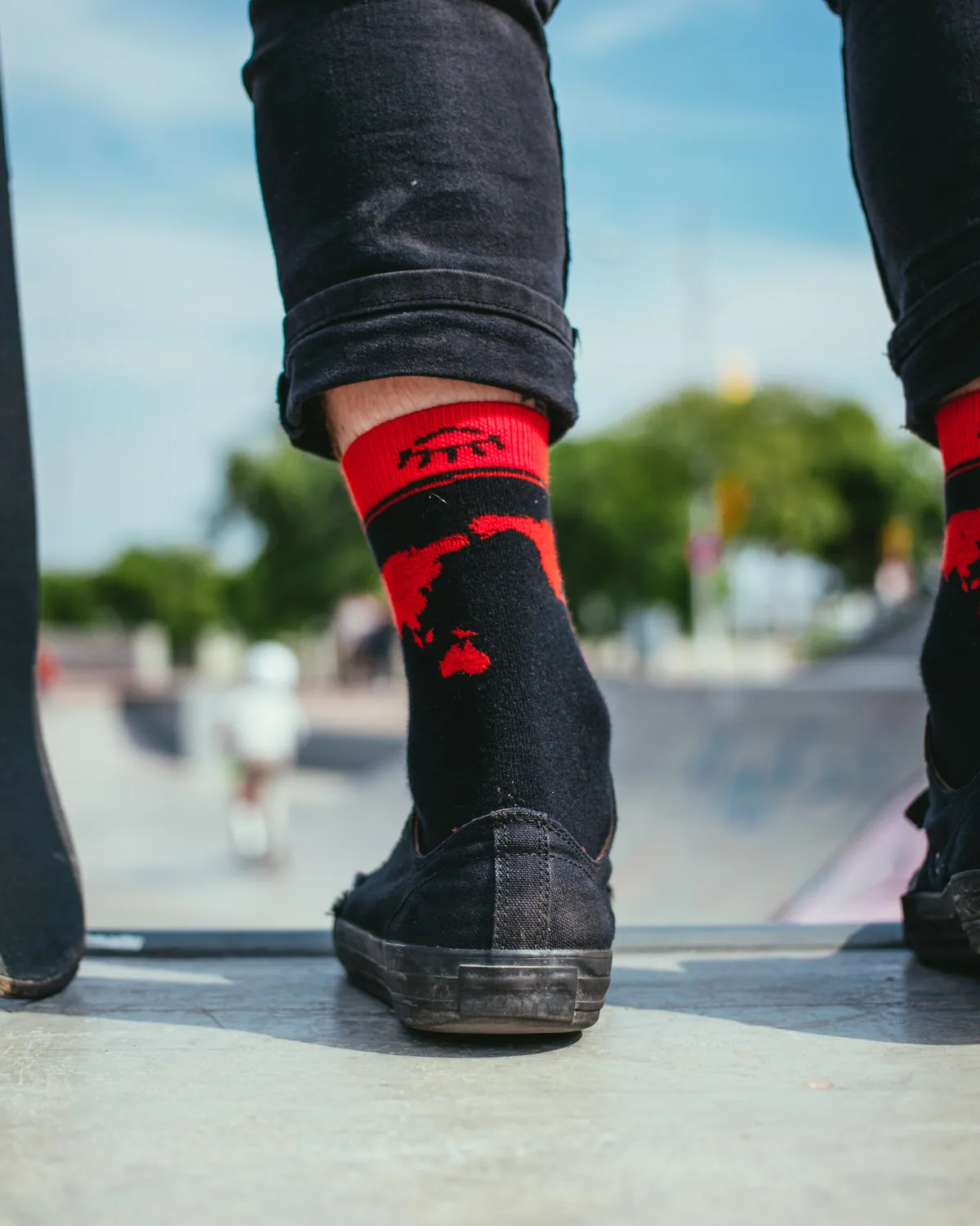 Black sneakers and red ribbed socks on a skateboard at a skatepark