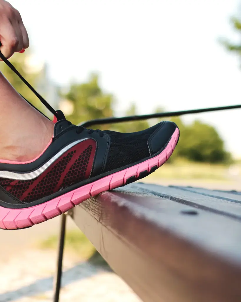 A black running shoe with a pink sole, laces being pulled tight