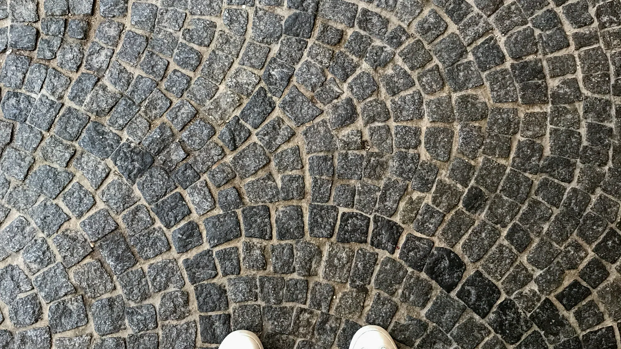 White sneakers seen from above on fan-patterned cobblestones