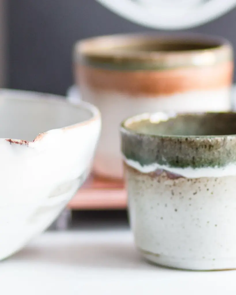 Two small speckled stoneware pots beside a chipped white bowl