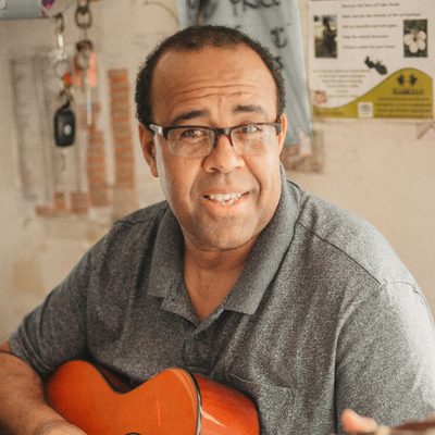 Danny Ferreira, who leads the church band, smiling with his acoustic guitar