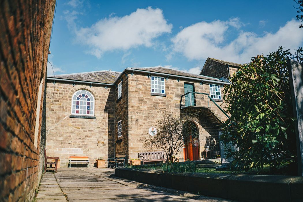 The sandstone church building and its courtyard on a bright spring day, the red door open onto the path