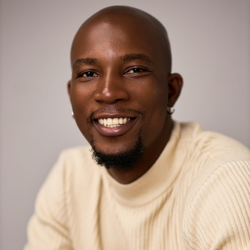 Danny Osei, head coach, smiling against a plain grey studio wall
