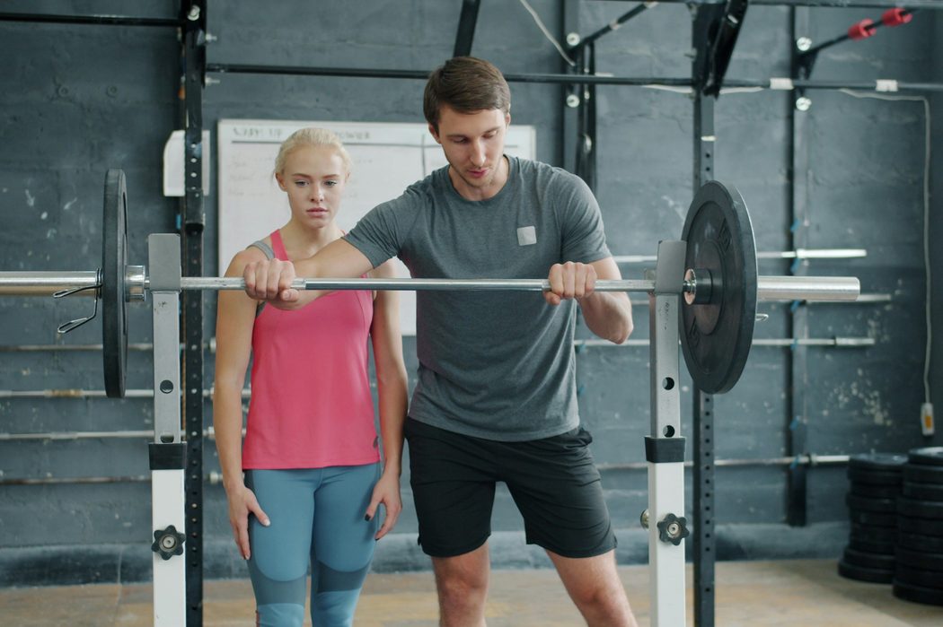 A coach adjusts a beginner's grip on the barbell at a squat rack in the Ironworks studio