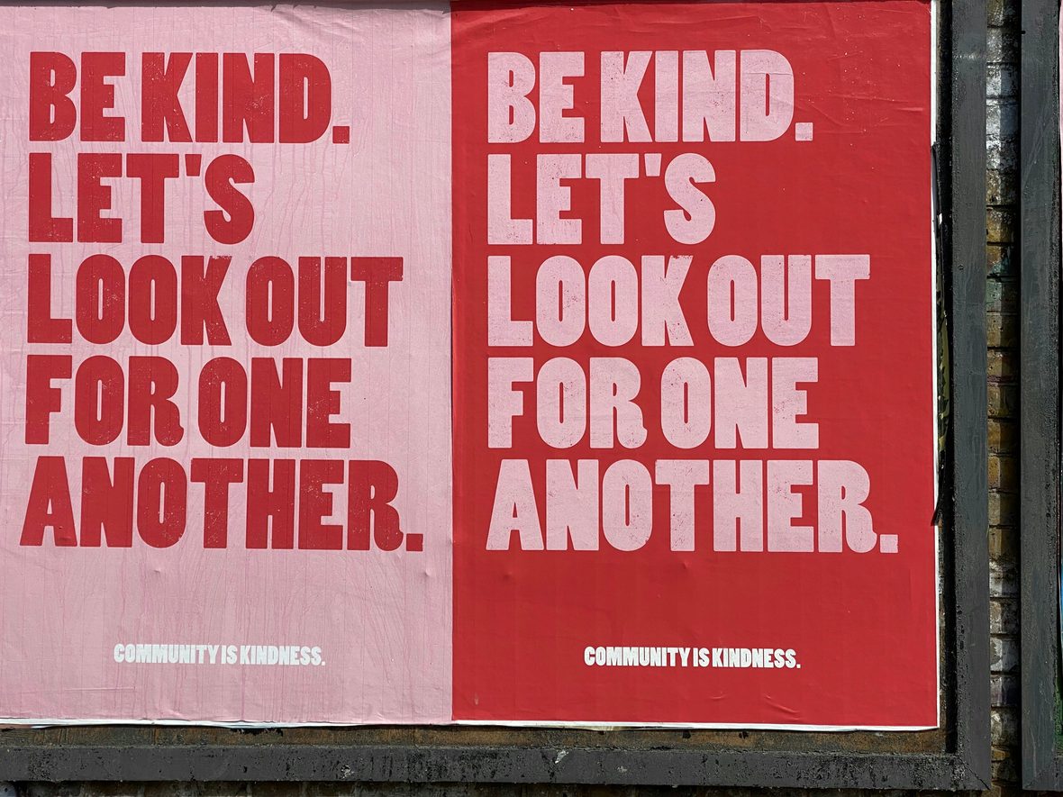 Common Ground campaign posters in pink and red pasted side by side on a street hoarding: "Be kind. Let's look out for one another."