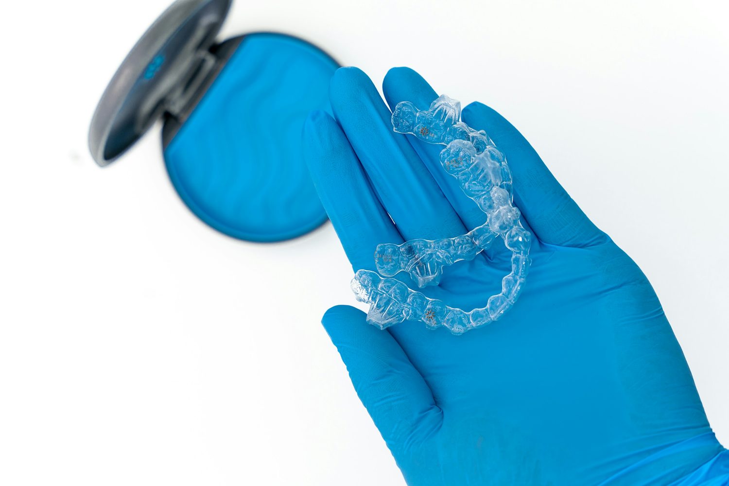 A clear aligner tray held in a gloved hand at Fore Street Dental, with the case it lives in open alongside