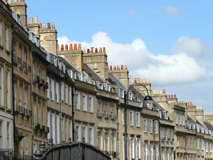 A row of Bath stone terraced houses with chimney stacks running downhill under a blue sky