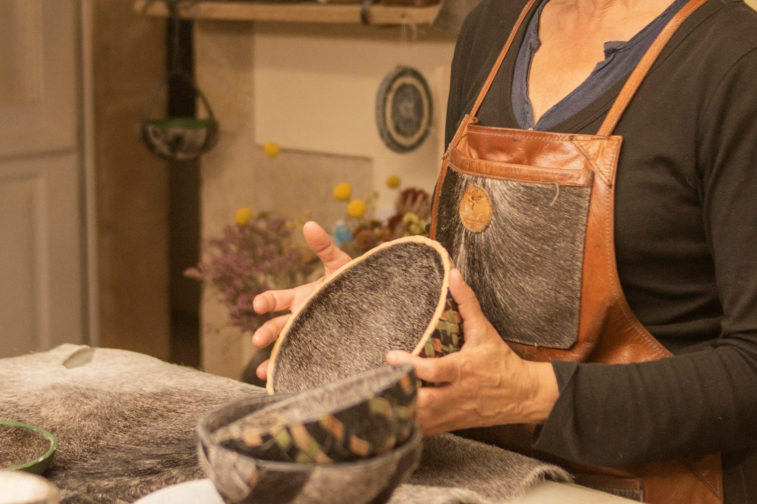 A maker in a leather apron turns a finished piece over in her hands at the bench before it leaves Rowan & Reed