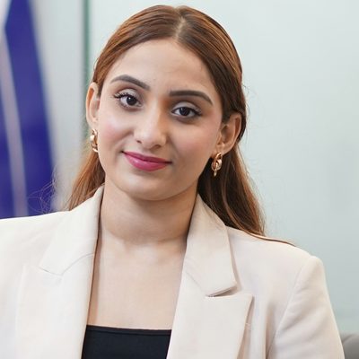 Aisha Rahman, Head of Growth at Unapp, in a cream blazer on the sofa of a bright glass-walled office