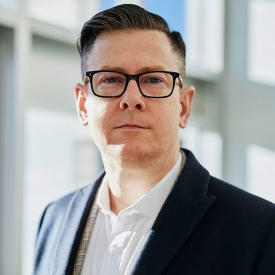Tom Alvarez, Engineering Manager at Vertex, in a dark blazer and glasses by an office window