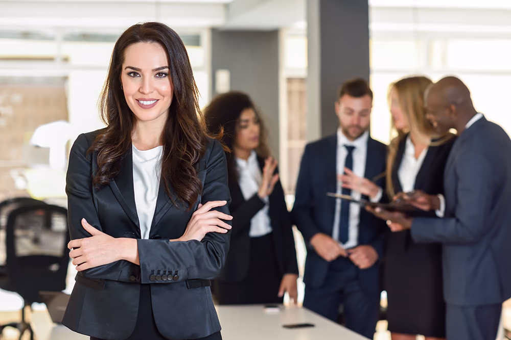 A smiling woman with her arms folded in front of colleagues in conversation