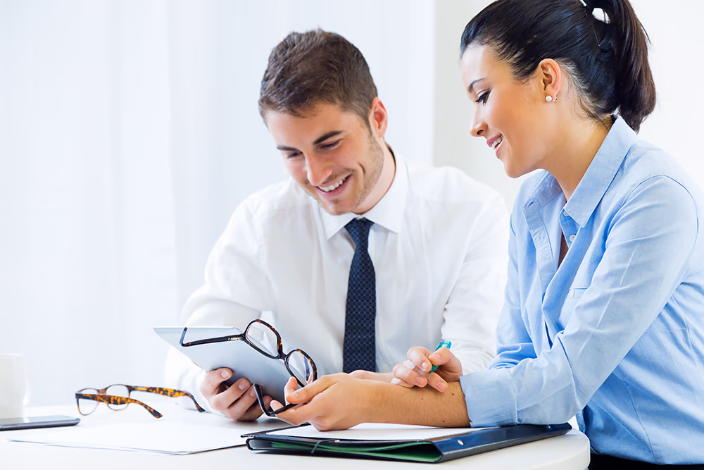 Two colleagues sitting side by side at a desk, looking over a document