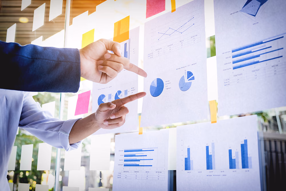 Hands pointing at charts and sticky notes on a glass wall