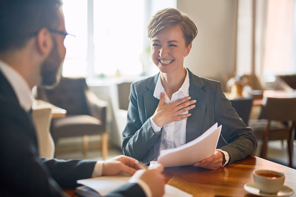 A woman holding papers and smiling during a meeting across the table
