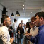 Attendees talking in small groups during a break, a man in a blue shirt explaining something to a man in glasses holding a glass